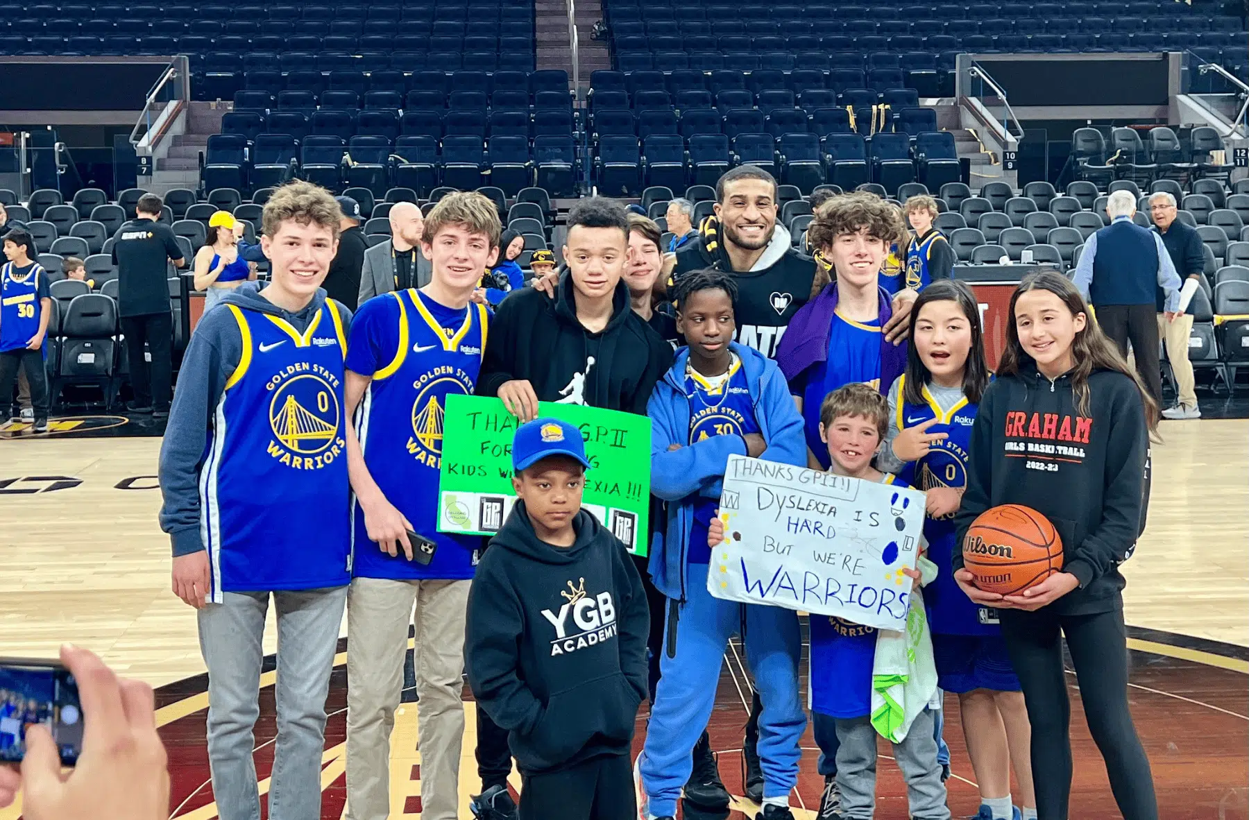 A group of young basketball fans posing with players at a game.
