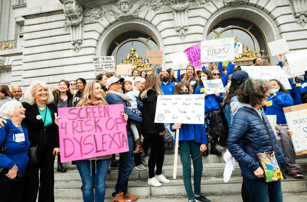 People protesting with signs about dyslexia awareness on steps.